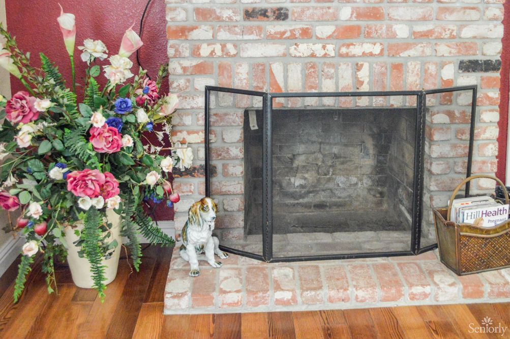 A cozy brick fireplace with a floral arrangement and a ceramic cat figurine.