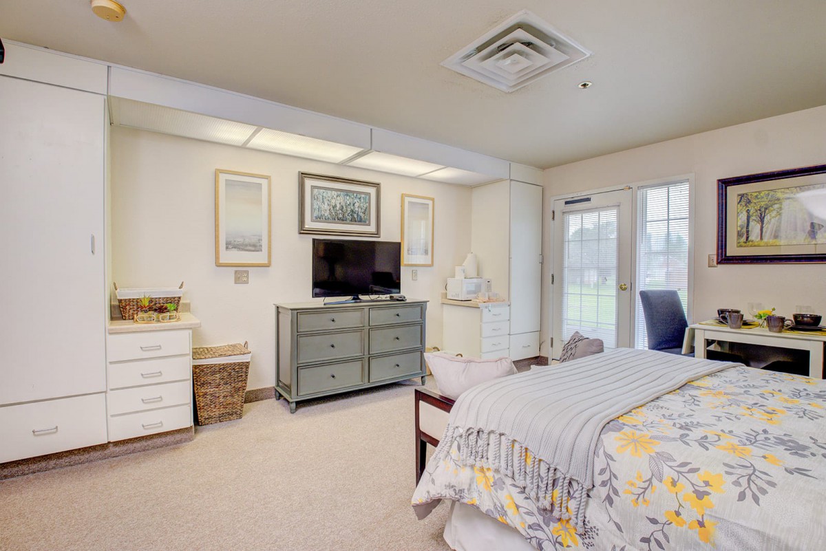 A cozy bedroom with a television on a dresser, adorned with artwork and comfortable bedding.