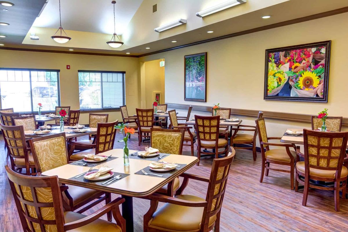 A well-arranged dining room with neatly set tables and comfortable chairs, illuminated by natural light through large windows.