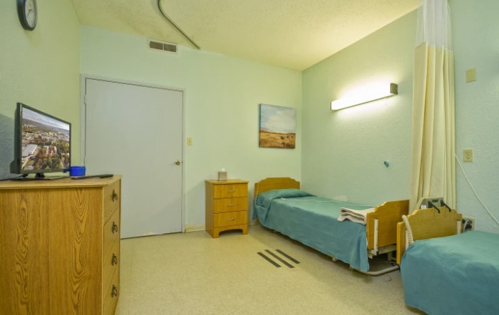 A simple hospital room with a bed and basic furniture.