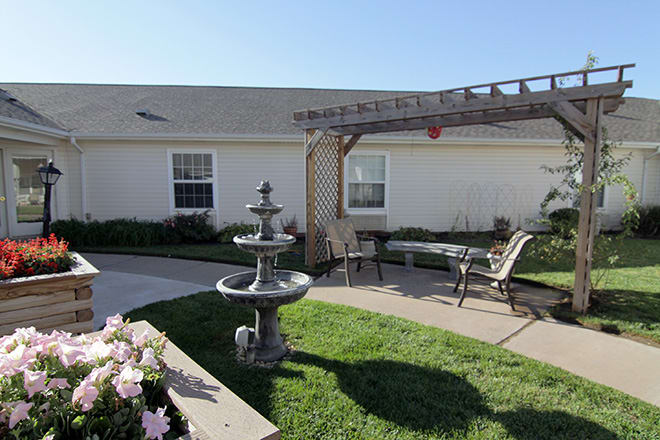 A tranquil garden patio with a central fountain, pergola, and seating area.