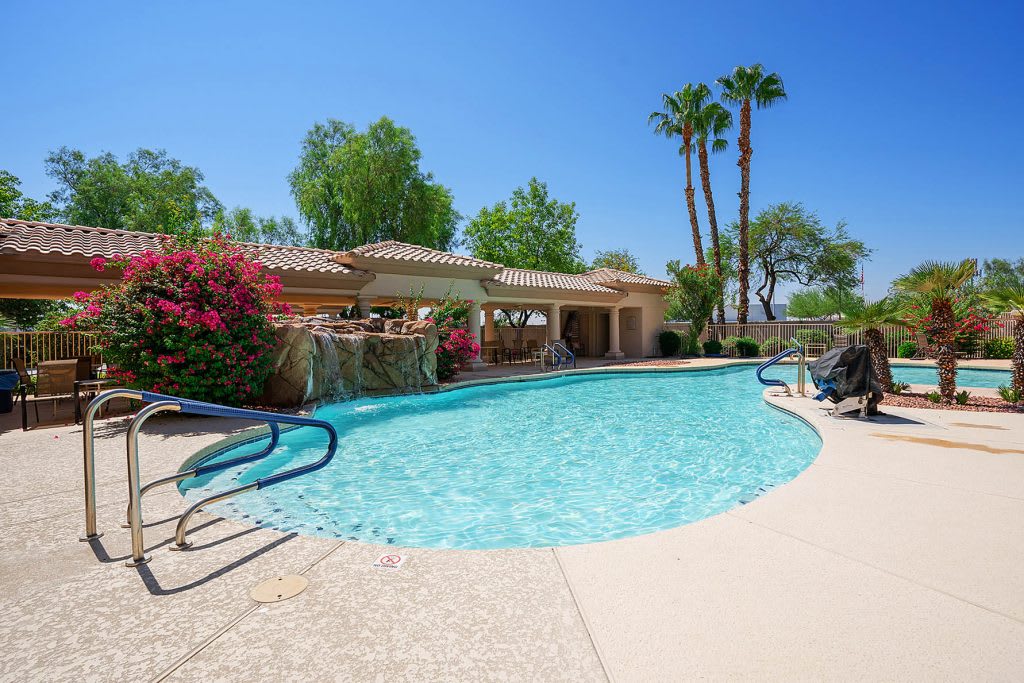 A serene outdoor swimming pool surrounded by lush greenery and palm trees on a sunny day.