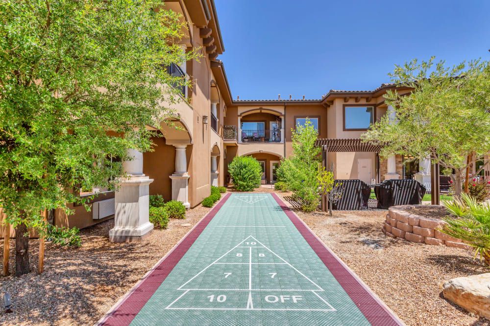Outdoor shuffleboard court surrounded by a building and landscape.