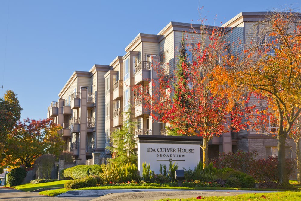 A residential apartment building with autumn trees and a clear blue sky.