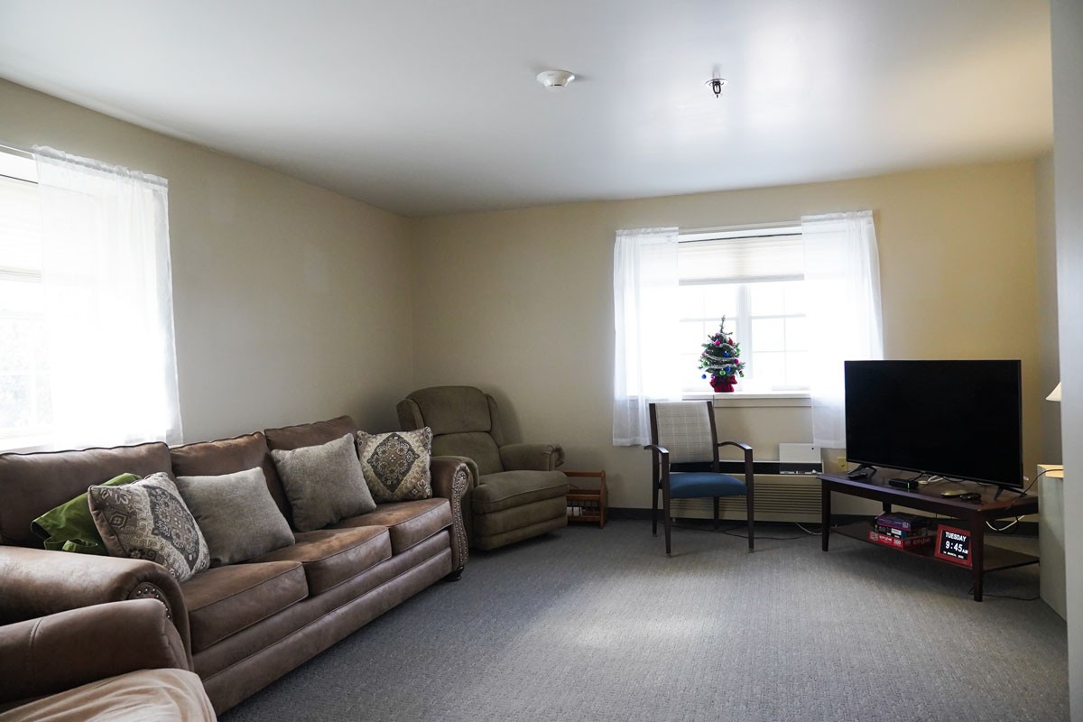 A cozy living room featuring a sofa, armchair, television, and a window with natural light.