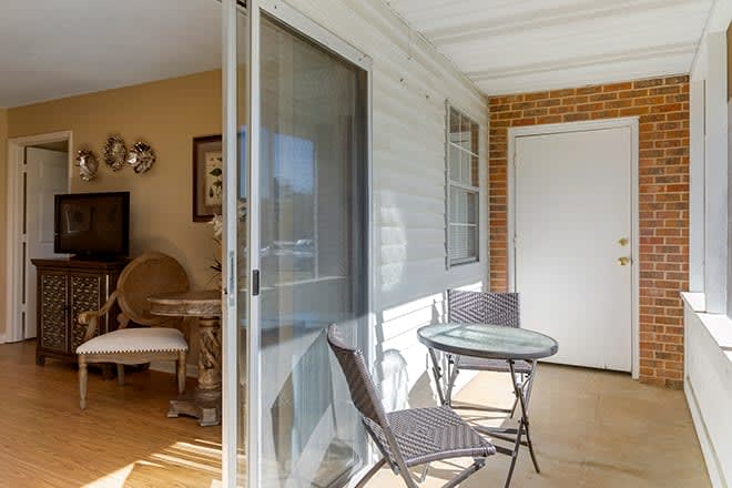A cozy porch with a small table and chairs, adjacent to a sliding glass door leading indoors.