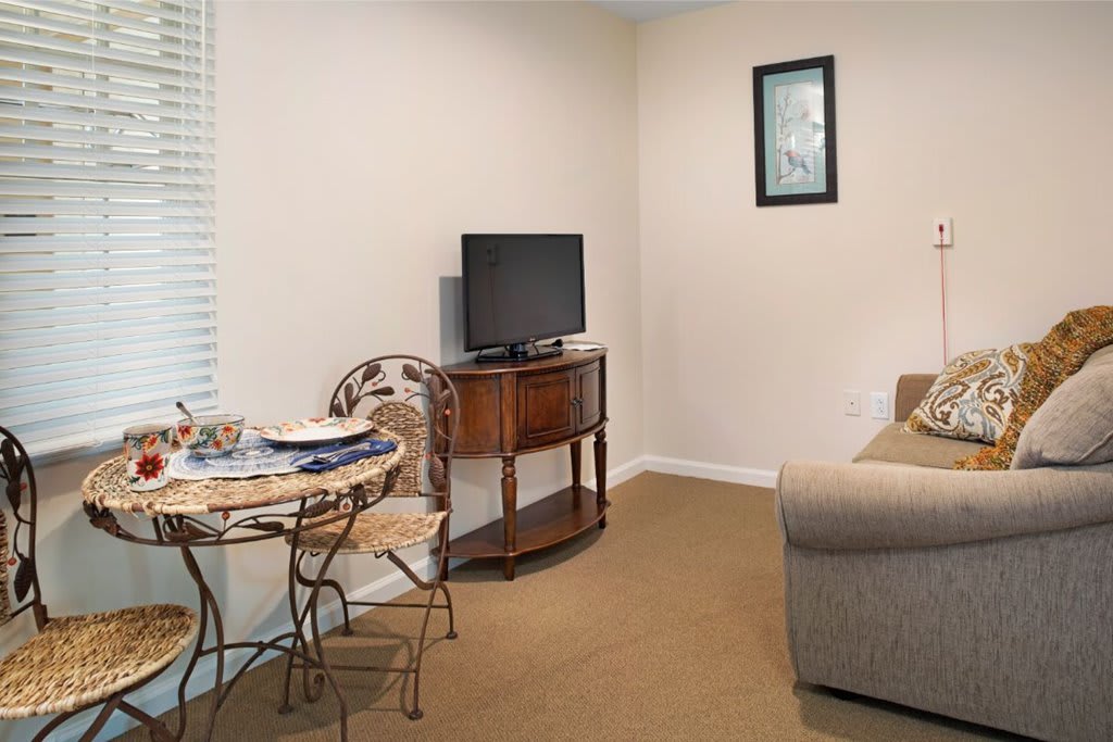 A cozy living room with a TV on a wooden stand, a sofa, and a small dining table with chairs.