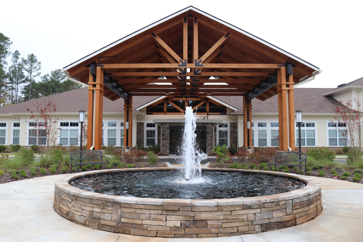 A beautifully designed building entrance with a central fountain, featuring wooden beams and landscaped surroundings.