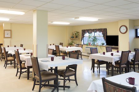 A well-lit dining area with neatly arranged tables and chairs, featuring white tablecloths.