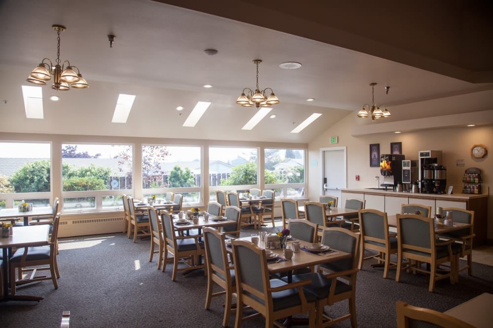 A bright dining area with tables and chairs arranged near large windows, allowing natural light to fill the space.