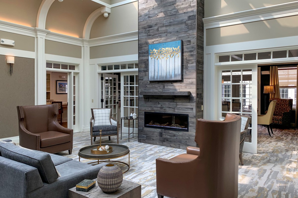 A modern living room featuring a tall stone fireplace, elegant seating, and large windows.