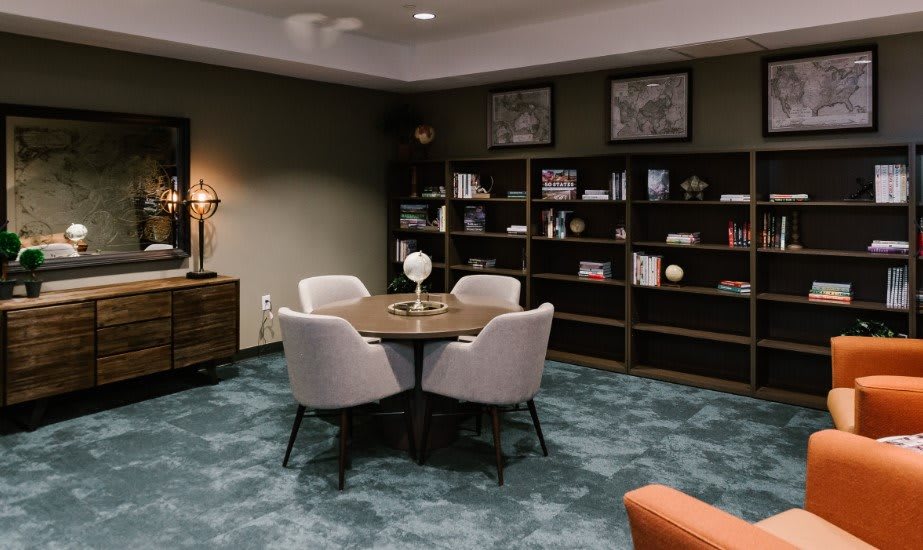 A cozy meeting room with a round table, four chairs, and bookshelves filled with books and decorations.