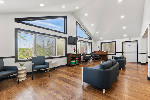 A modern lounge area featuring large windows for ample natural light, stylish furniture, and a warm wooden floor.