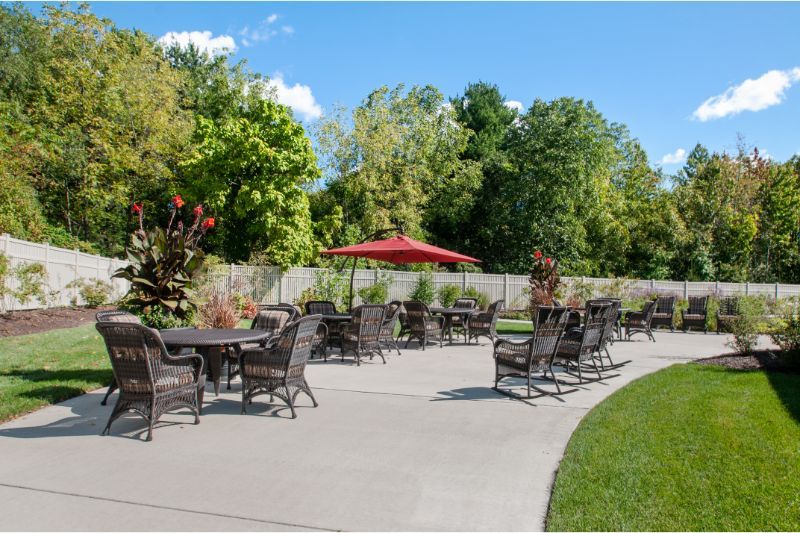 A peaceful outdoor patio with tables and chairs, surrounded by lush greenery on a sunny day.