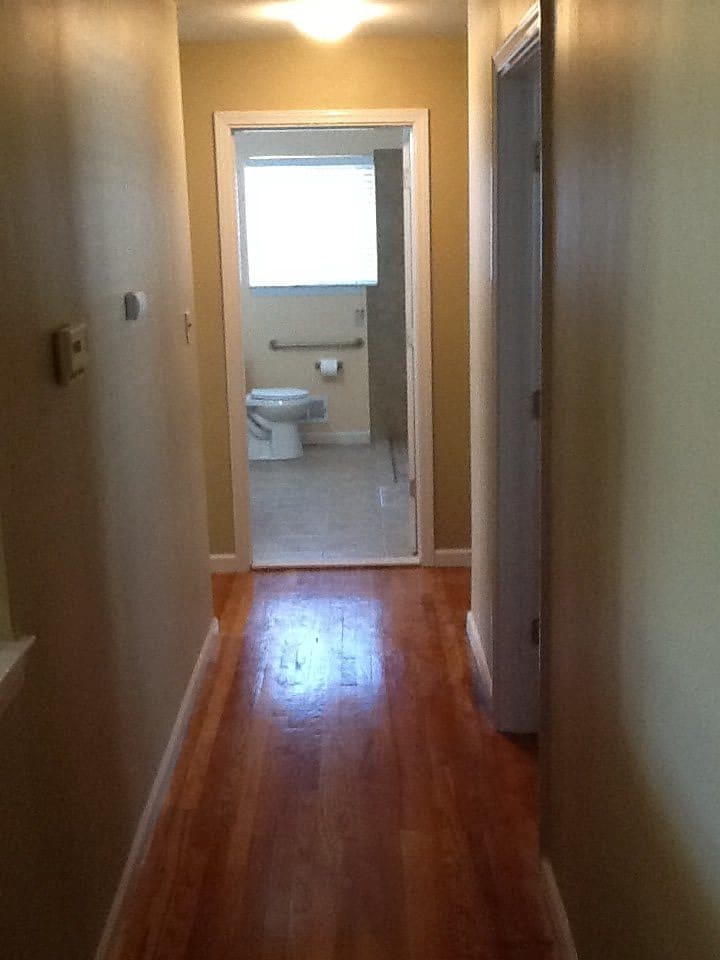 A view of a hallway with a wooden floor leading to a bathroom.