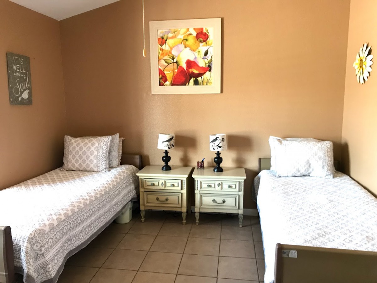 A cozy bedroom featuring two twin beds with matching nightstands and decorative lamps, complemented by a floral painting on the wall.
