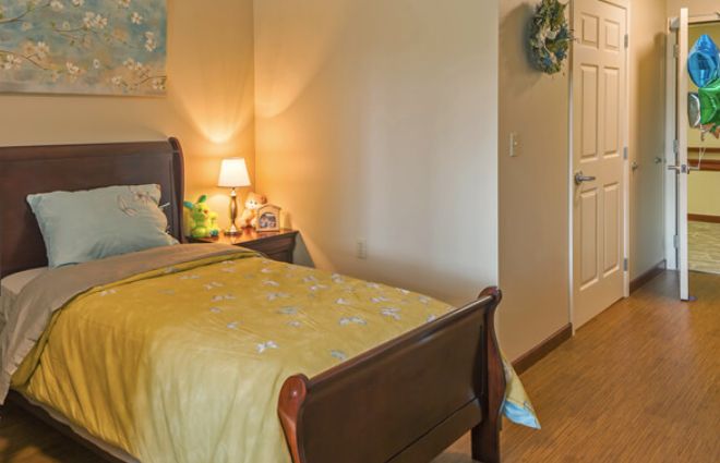 A cozy bedroom featuring a bed with yellow bedding, a nightstand with a lamp, and decorative elements.