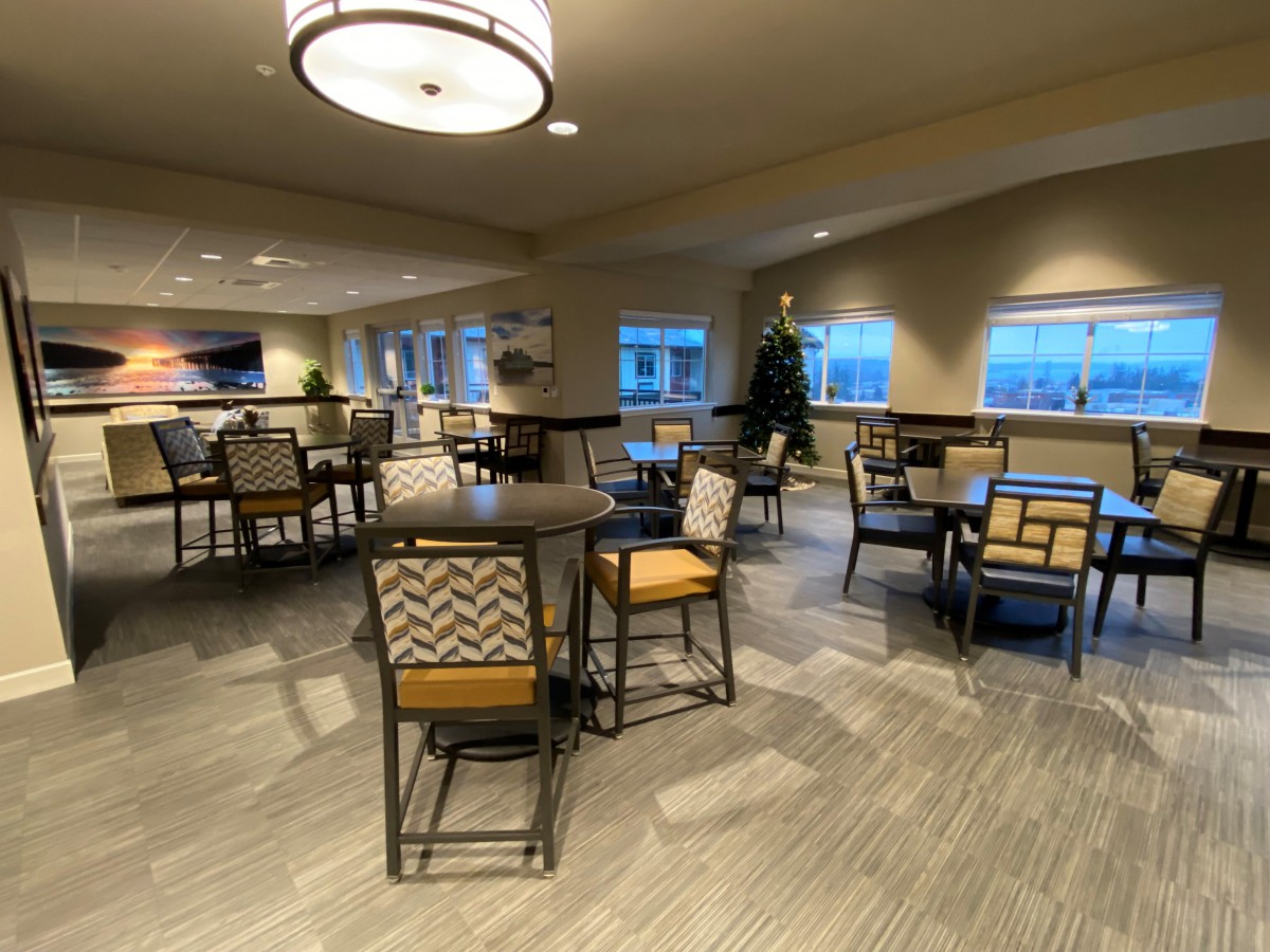 A cozy indoor dining area with tables and chairs, warmly lit with natural light from the windows.