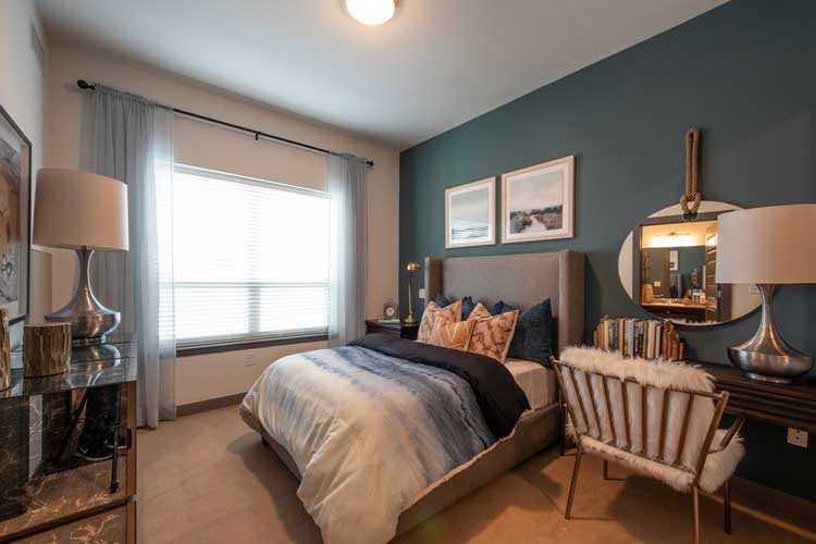 A modern bedroom with stylish decor, featuring a neatly made bed, decorative pillows, and a large window letting in natural light.