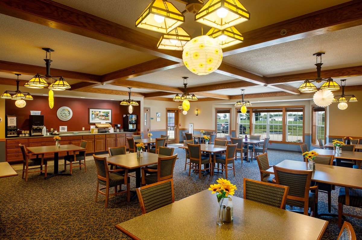 A cozy dining area with wooden tables, comfortable chairs, and warm lighting fixtures.