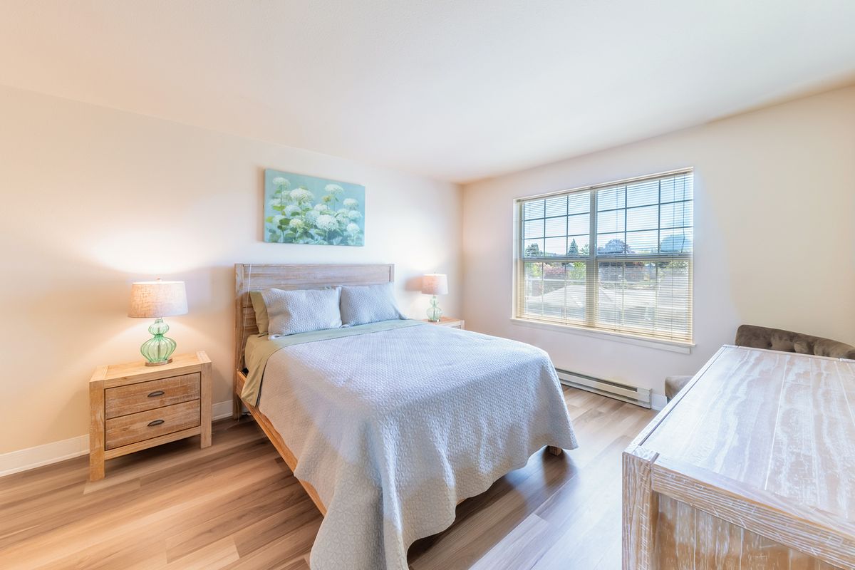 A bright and cozy bedroom featuring a neatly made bed, two bedside tables with lamps, and a large window allowing natural light to fill the room.