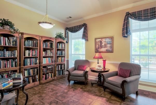 A cozy reading room with bookshelves and comfortable armchairs, softly lit by a table lamp.