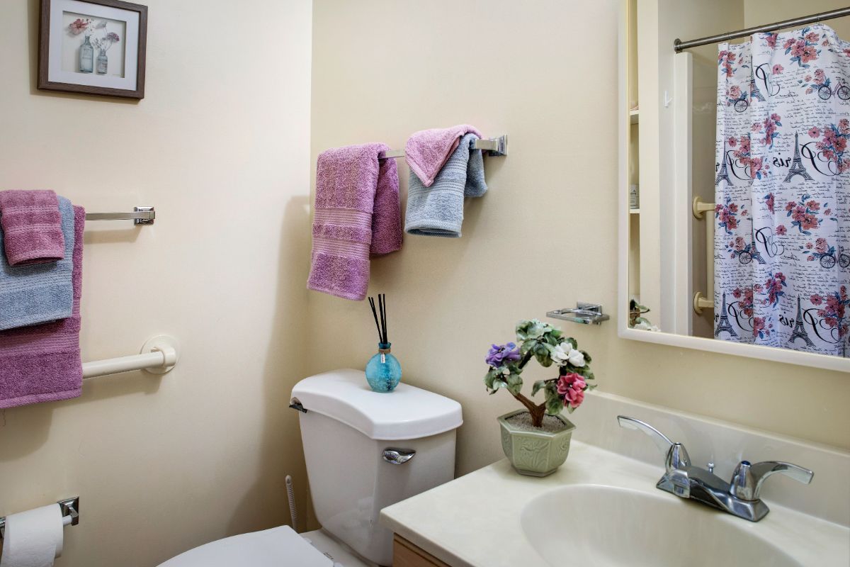 A neatly arranged bathroom with a sink, mirror, toilet, and colorful towels.