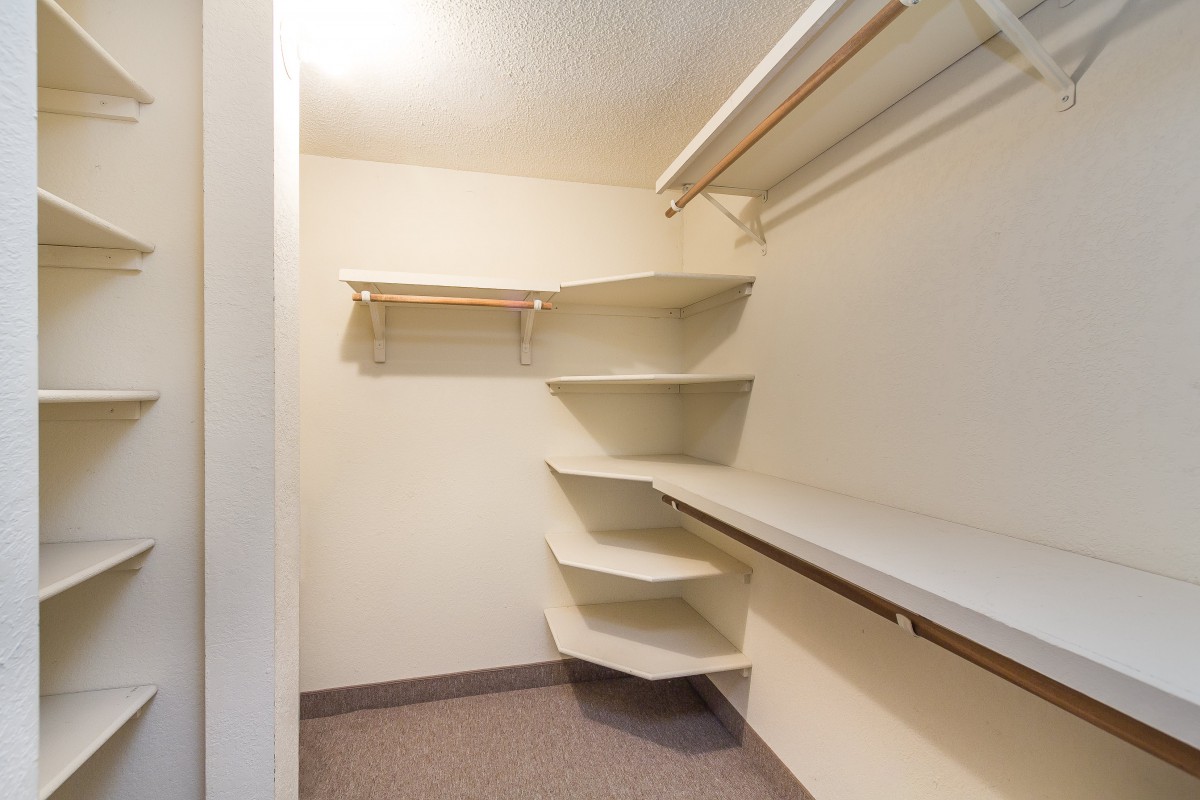 An empty walk-in closet with corner shelves and hanging rods.