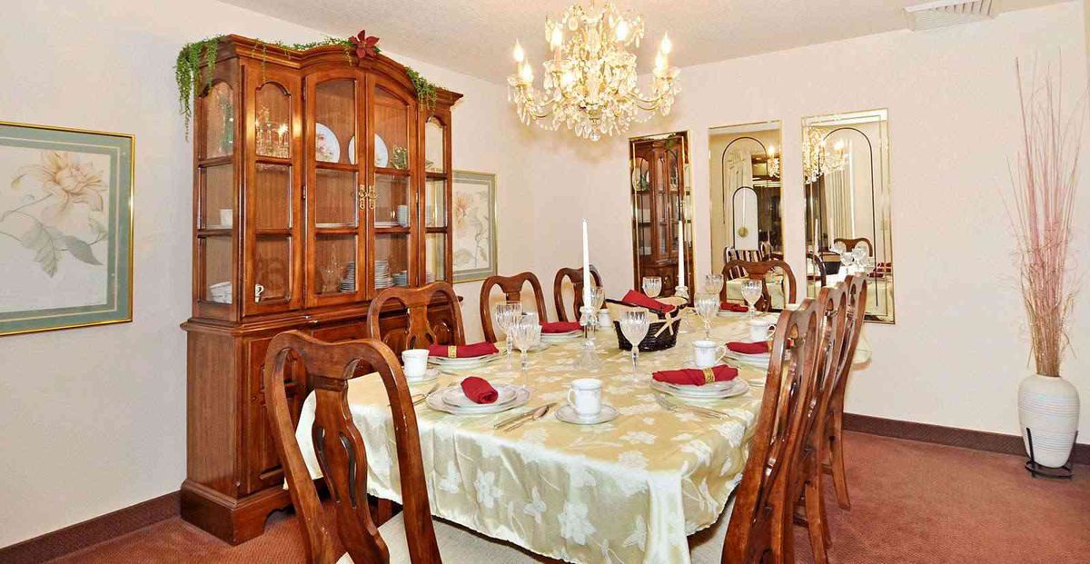 An elegantly decorated dining room featuring a large table with ornate chairs, a sparkling chandelier, and a china cabinet filled with dishes.
