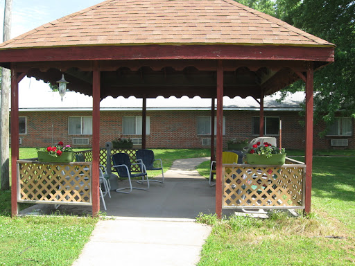 A cozy gazebo surrounded by greenery, featuring seating and vibrant flowers.