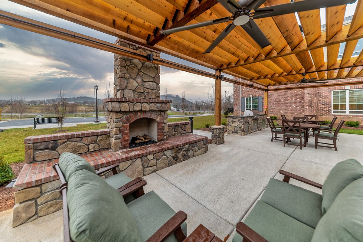 A cozy outdoor patio with a stone fireplace and comfortable seating under a pergola.
