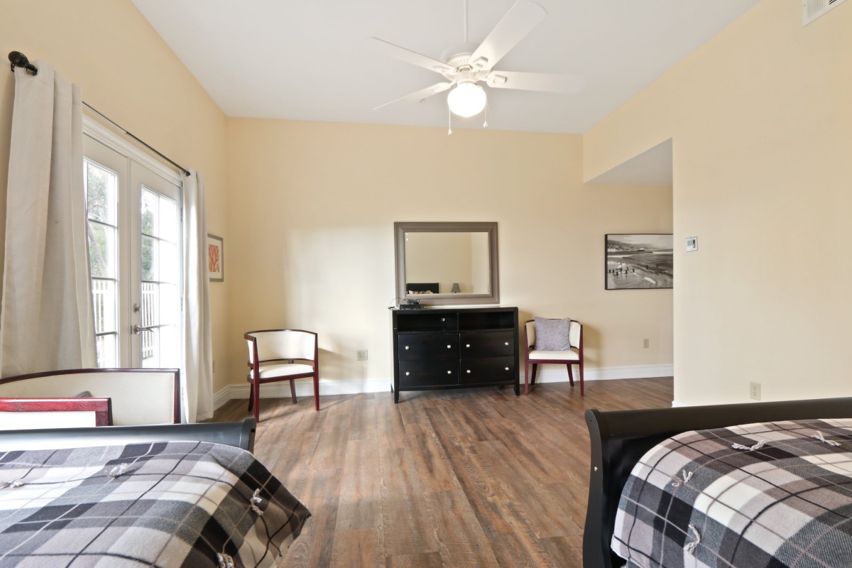 A minimalist bedroom featuring a wooden floor, dresser with mirror, and two chairs.