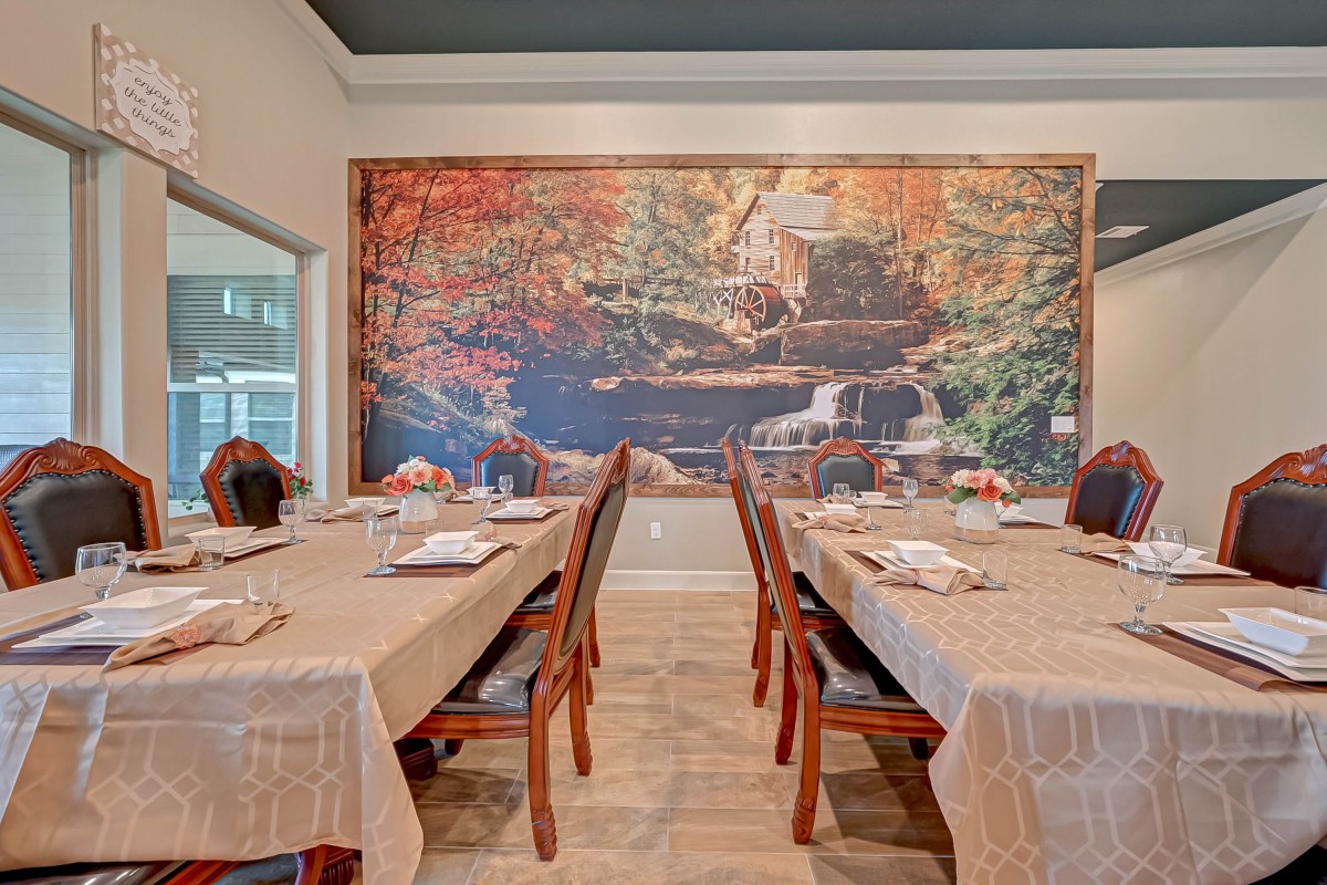 A cozy dining room with two tables covered in tablecloths, set against a large mural depicting a scenic landscape.