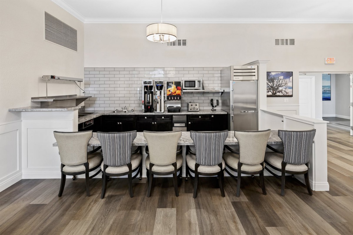 A modern kitchen interior featuring a long dining counter with multiple chairs and sleek appliances.