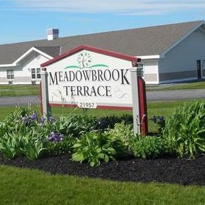A sign for Meadowbrook Terrace set amidst a landscaped garden in a residential community.