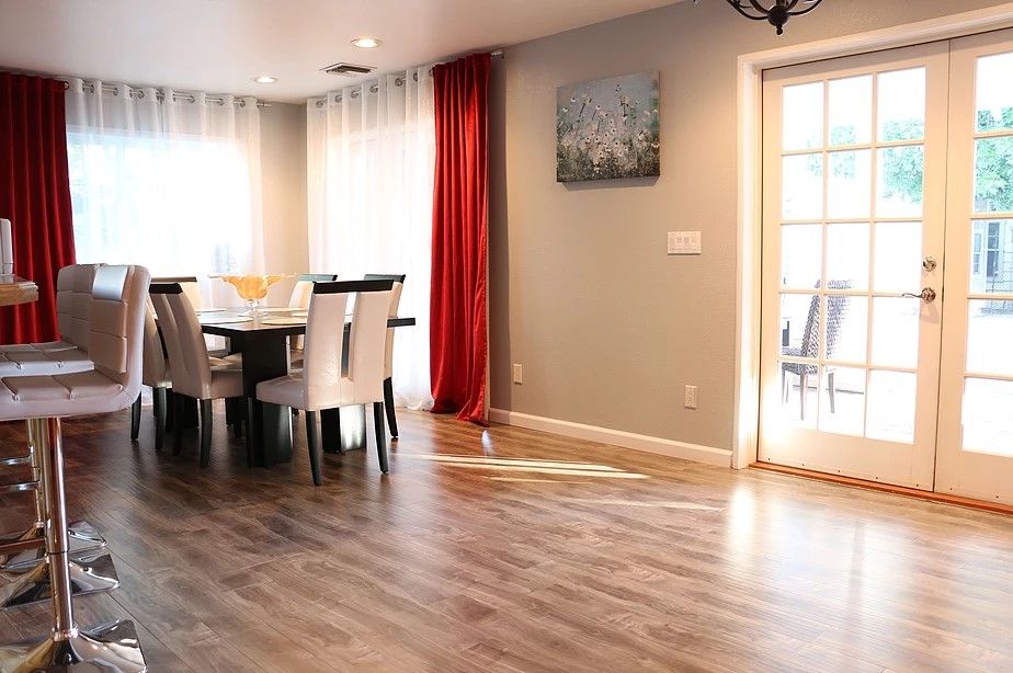 A well-lit dining area with wood flooring, featuring a table and chairs, complemented by curtains and wall art.