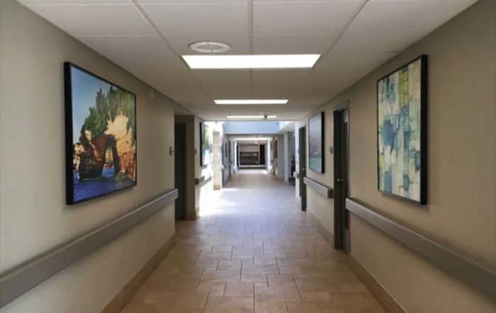 A hospital hallway with art-lined walls and bright lighting leading to another section.