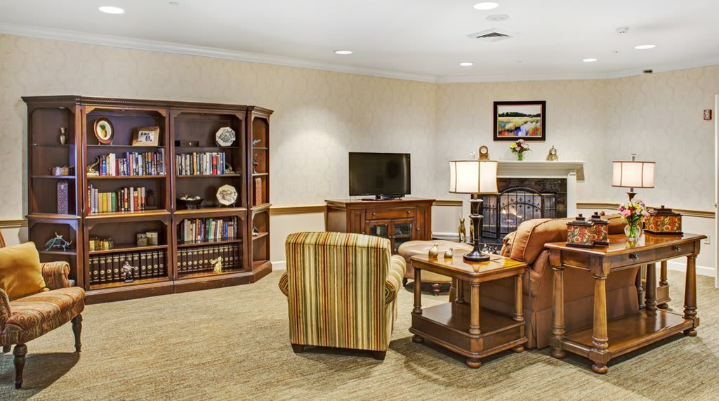 A cozy living room with a television, bookshelf, and comfortable seating around a fireplace.