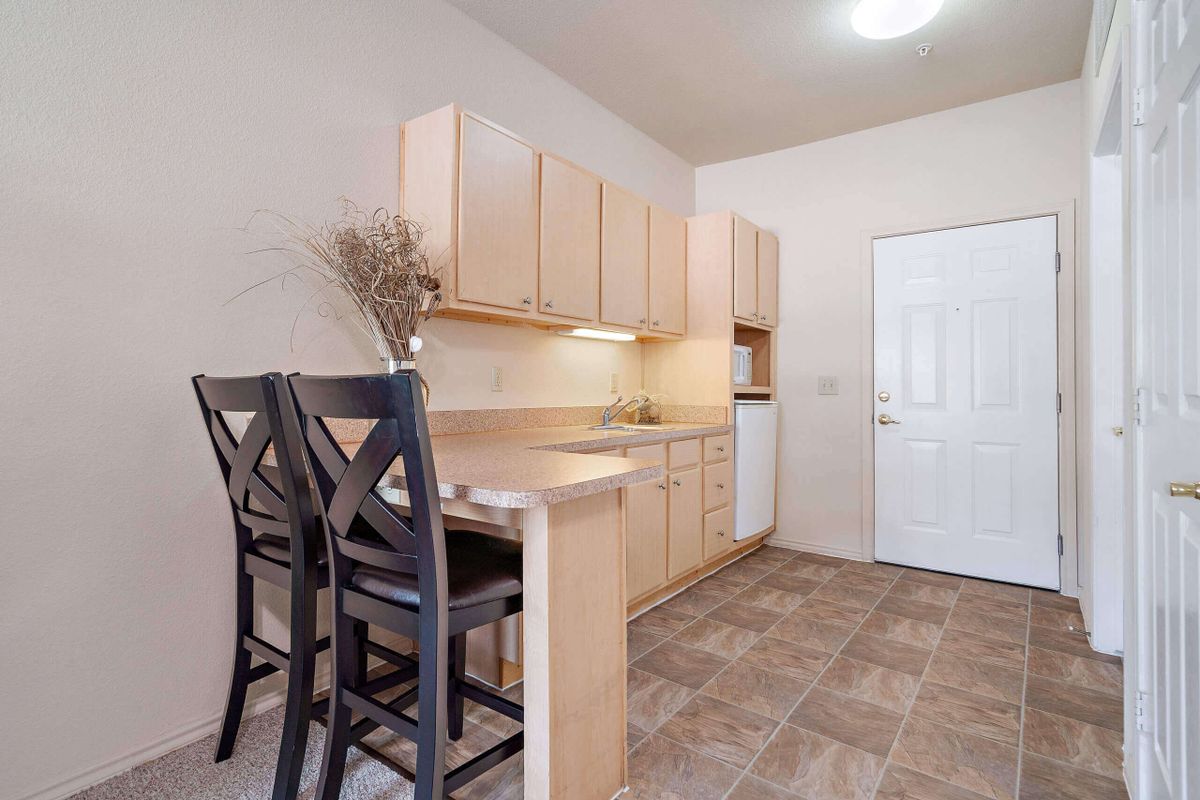 A compact kitchen area with light wood cabinets, barstools, and a tile floor.