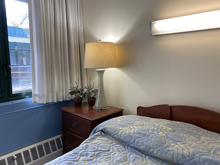 A cozy bedroom setup featuring a bedside lamp, nightstand, and light-colored bedding.