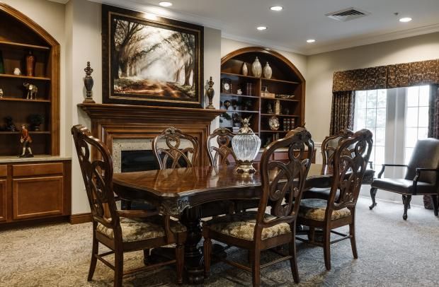 An elegant dining room with wooden furniture, featuring a table and chairs, a fireplace, a painting, and built-in shelves.