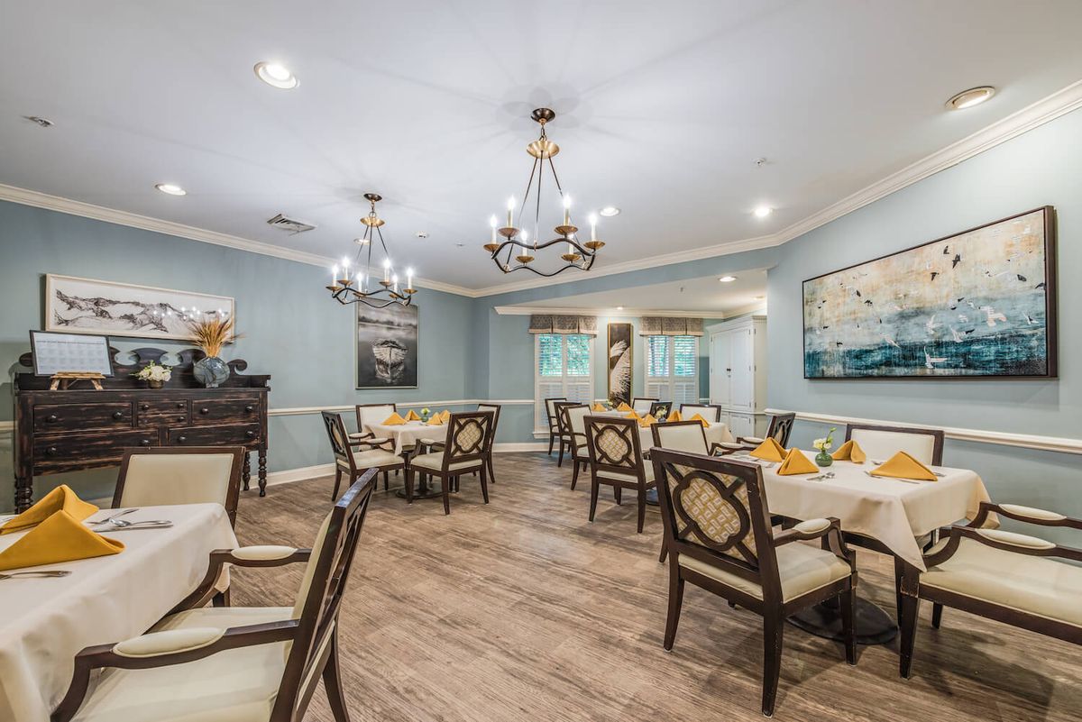 An elegantly designed dining room featuring chandeliers, arranged tables and chairs, with decorative artwork on the walls.