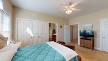 A cozy bedroom featuring a bed with a teal cover, a ceiling fan, and a TV.