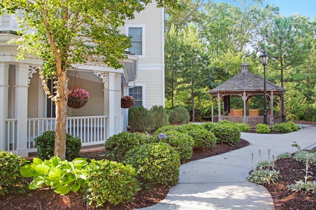 A scenic garden with a winding pathway and a gazebo beside a house.