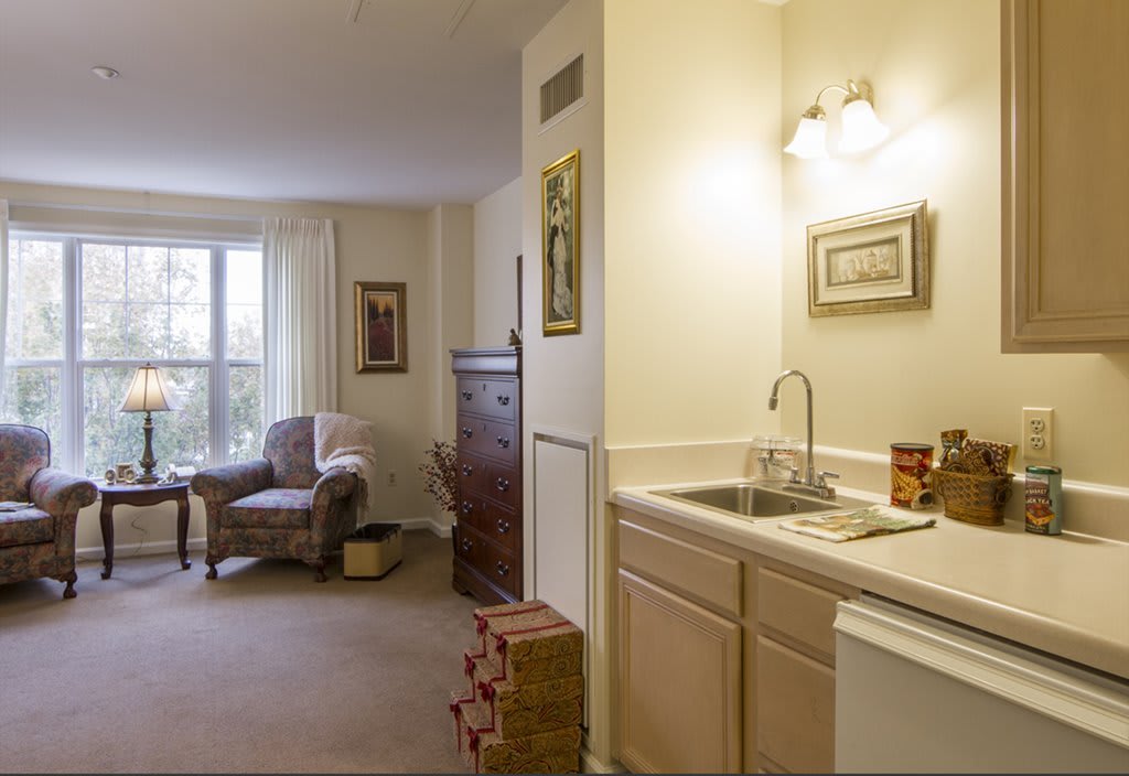 A cozy living area with a kitchenette, armchair, and dresser.