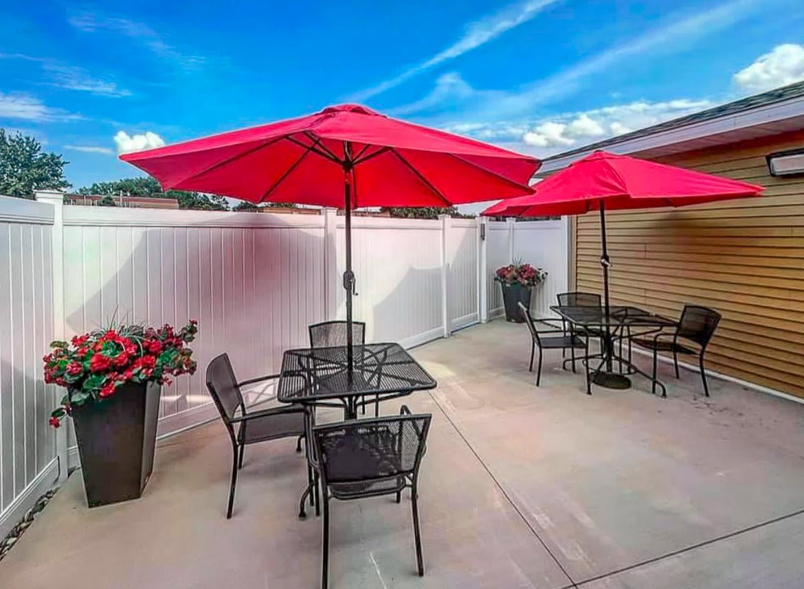 A sunny outdoor patio with red umbrellas and metal furniture.