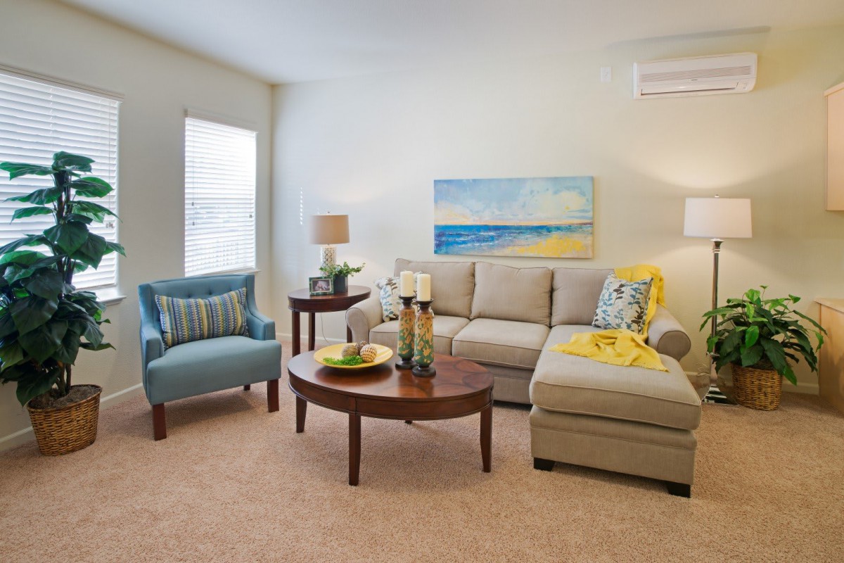 A cozy living room with a beige sectional sofa, a blue armchair, and a wooden coffee table, featuring decorative elements and wall art.