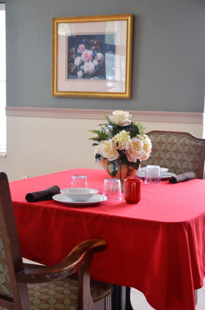 A dining table set with a red tablecloth, adorned with a bouquet of flowers, plates, glasses, and napkins.