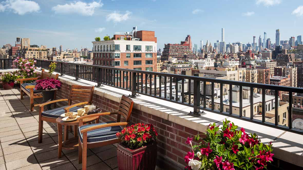 A rooftop terrace with a view of the city skyline, featuring outdoor seating and vibrant plants.