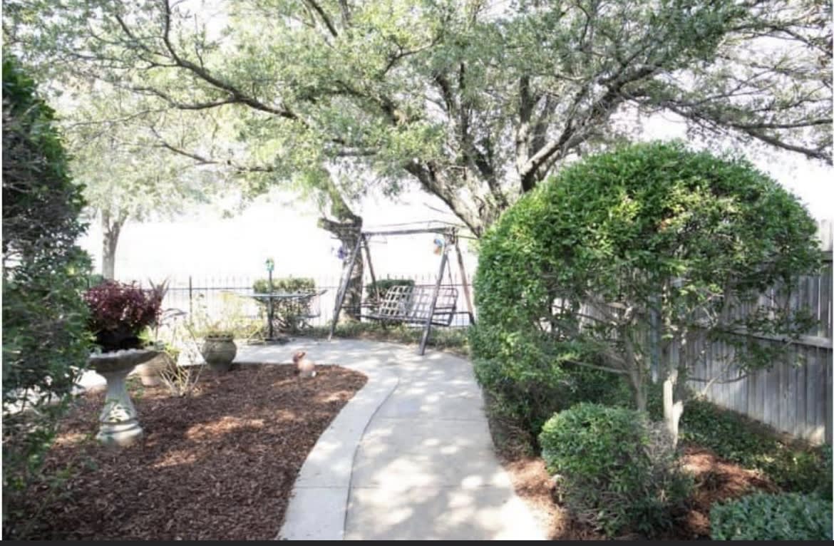 A serene garden pathway surrounded by trees and shrubs, leading to a swing set.